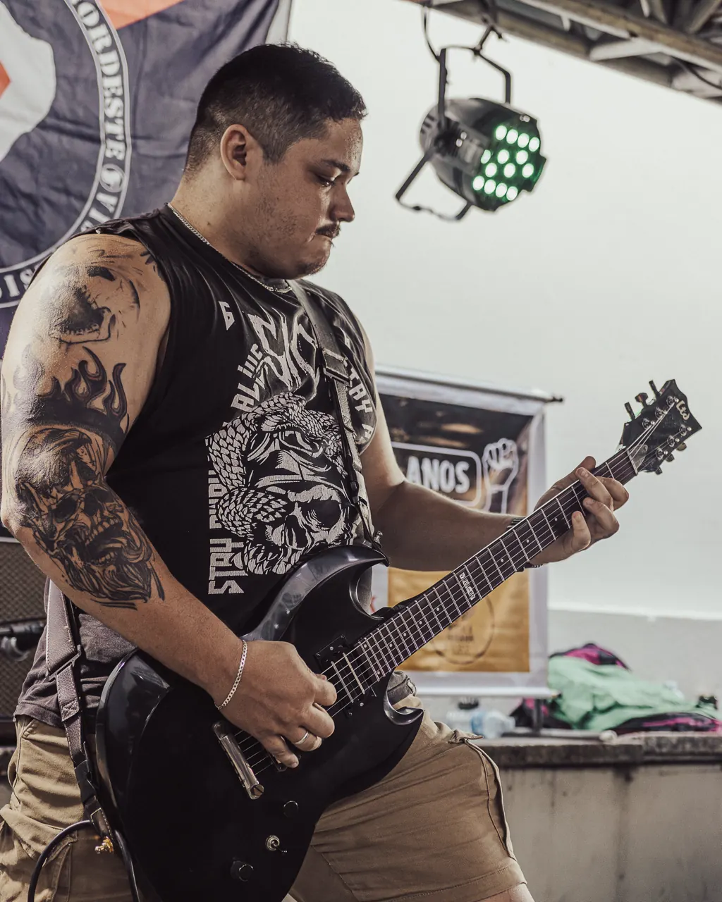 Guitarrista de regata toca sob a luz verde de um refletor.
