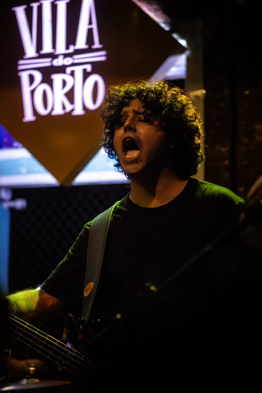 Músico de cabelo cacheado grita, com a placa do Vila do Porto acima.